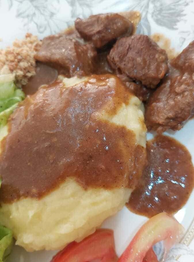Foto, com zoom aproximado para mostrar a textura, da carne e do molho acompanhada com purê de batata.